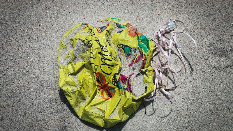 A burst yellow balloon and tangled ribbon lying on wet sand.