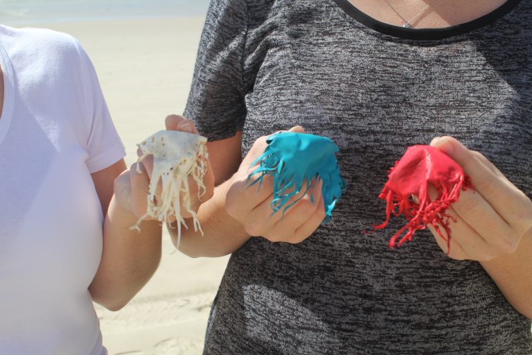 Burst balloons laid out on sand after a beach collection.